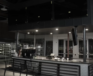 Empty bar counter in a modern café at night, with stools along the tiled counter and equipment in the back area.