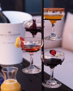 Assorted cocktails in coupe glasses on a metal stand with citrus and berry garnishes.