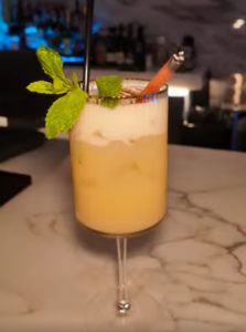 Cocktail in a stemmed glass on a marble bar, garnished with fresh mint and a straw.