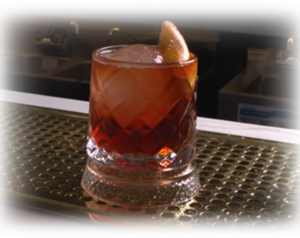 Amber cocktail in a faceted glass with an orange twist garnish, set on a perforated bar counter.
