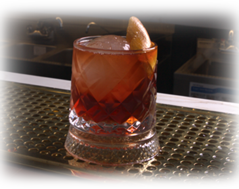 Amber cocktail in a faceted glass with an orange twist garnish, set on a perforated bar counter.
