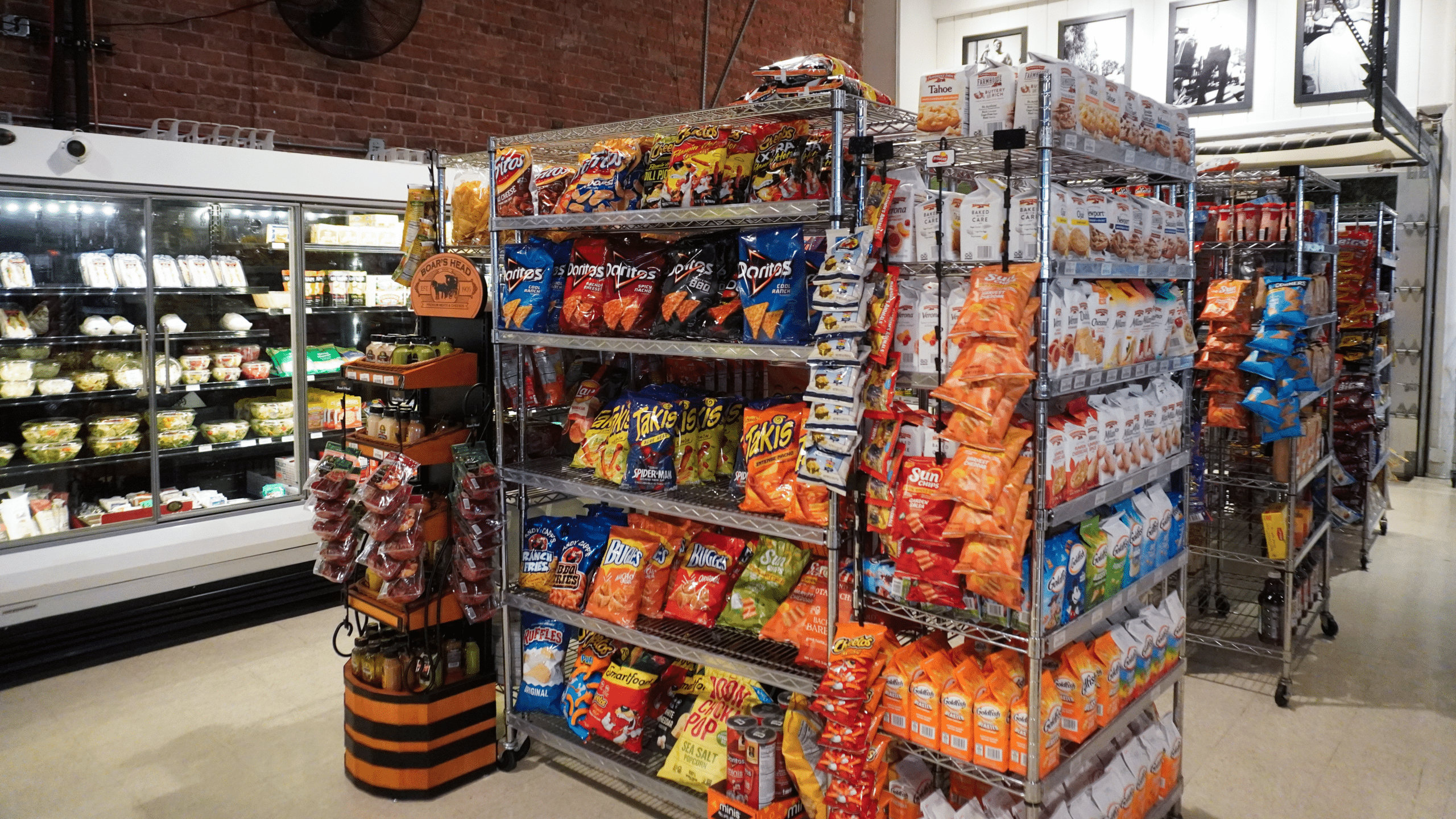 A grocery store aisle with tall metal shelves stocked with chips and snacks beside refrigerated cases.