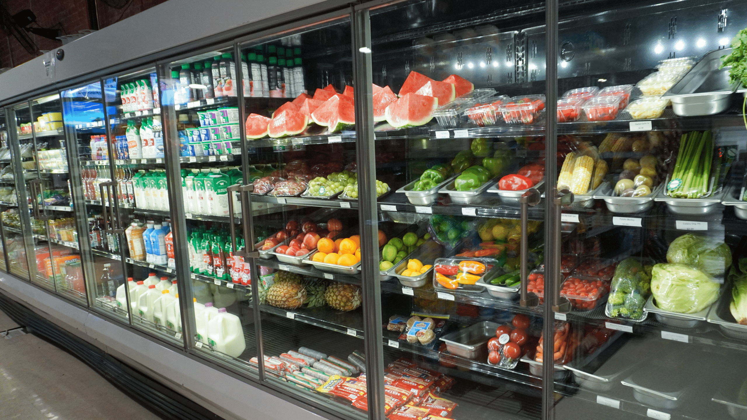 Row of pre-packaged deli sandwiches on a refrigerated shelf, with clear plastic containers and labels visible on each pack.